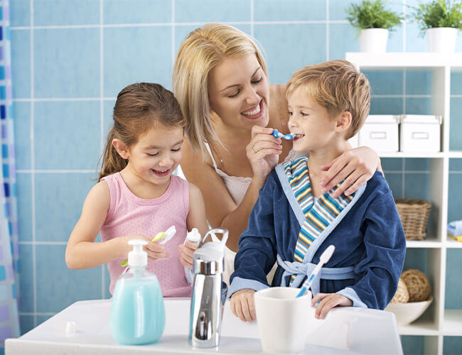 A mom showing her son and daughter how to brush their teeth