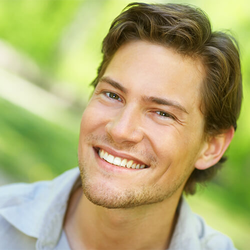 Close up of a young man with a beard smiling outdoors