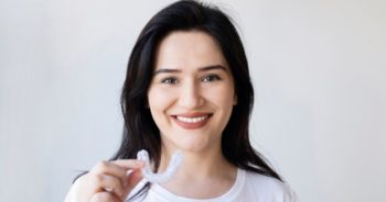Woman smiling and holding up an Invisalign aligner.